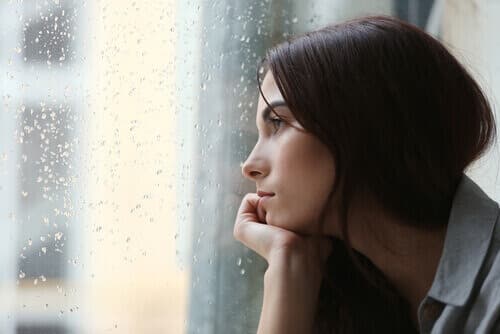 Woman with depression looking out the window with raindrops on the glass