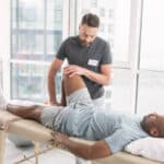 man lying on physical therapy table with therapist moving his lower leg