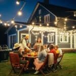 family and friends sitting around outdoor table with food next to house in evening