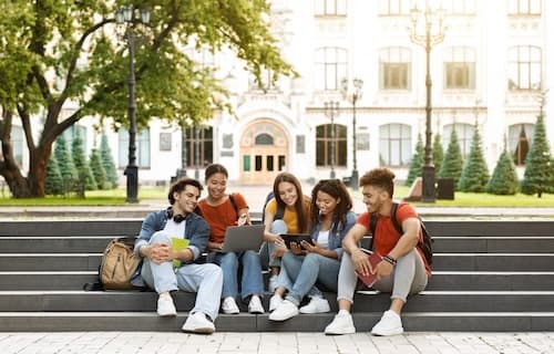 Group of college students sitting on campus steps looking at laptop and tablet