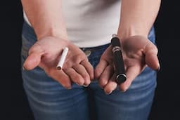 Unrecognizable woman holding vape and tobacco cigarette in hands.