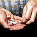 Heap of colorful medical pills in senior male hands closeup.